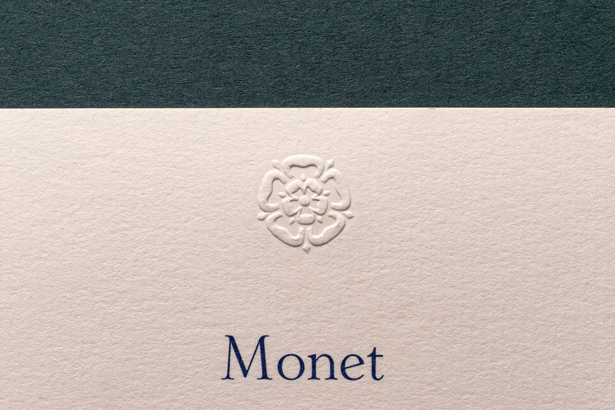 an embossed motif of a flower shape on a high quality premium business card with the word Monet printed in blue