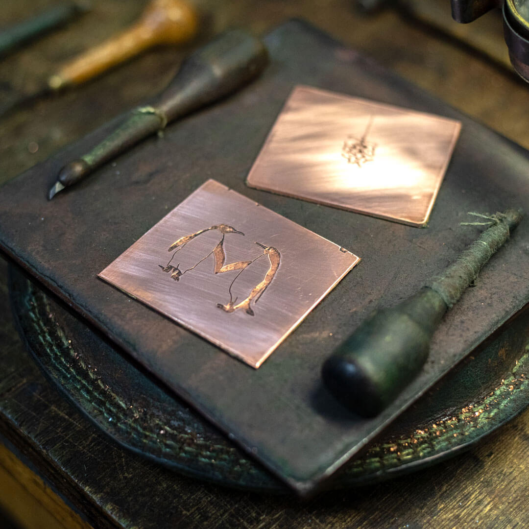a copper plate hand engraved with a penguin design surrounded by tools