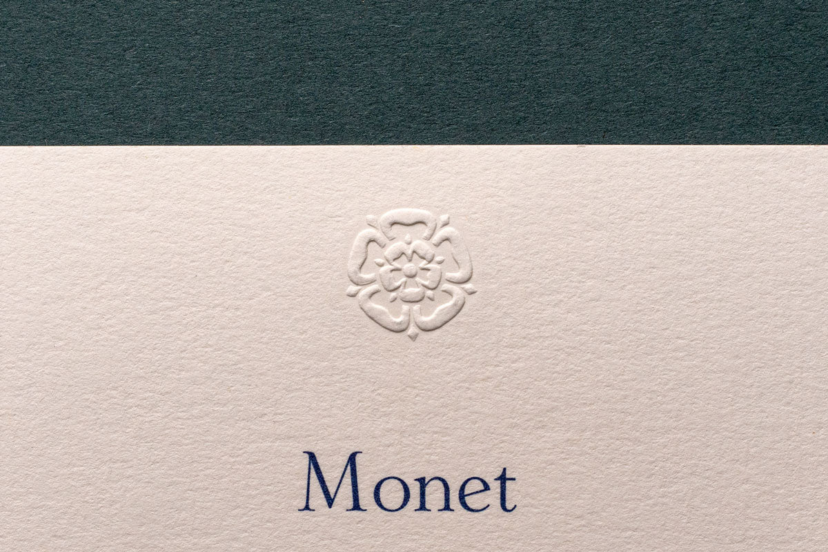 an embossed motif of a flower shape on a high quality premium business card with the word Monet printed in blue
