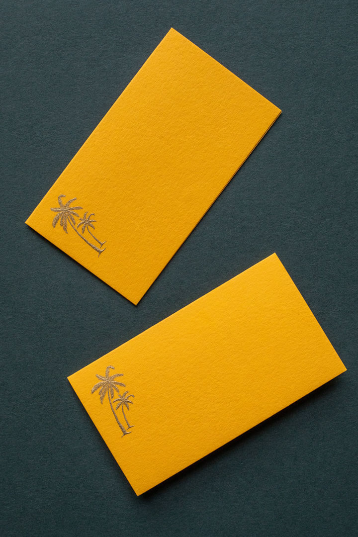 a high end bright orange business card with a hand engraved die stamped logo of a palm tree in gold